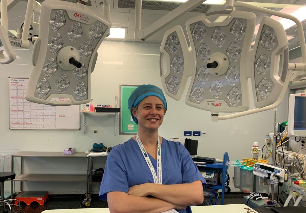 Dr Amy Garner, smiling with arms folded, standing in an operating theatre.