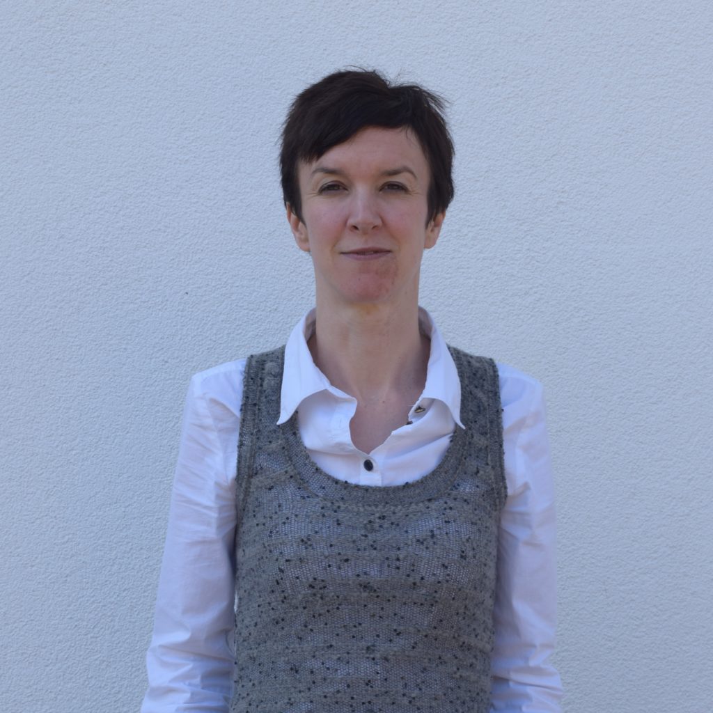 Dr Alison Yarnall (white woman with short brown hair) wearing a white shirt and standing against a white wall.