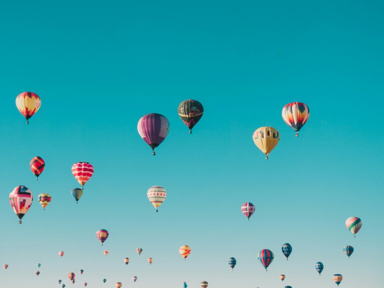 A large group of hot air balloons rising against a blue sky.